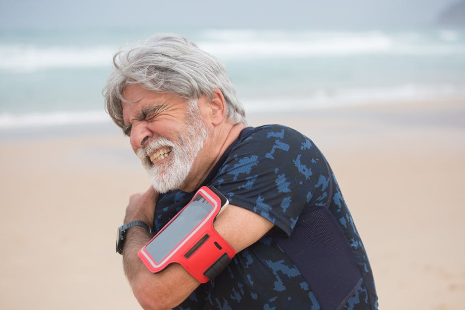 Elderly man grimacing from shoulder pain during seaside walk, showcasing health issue outdoors.
